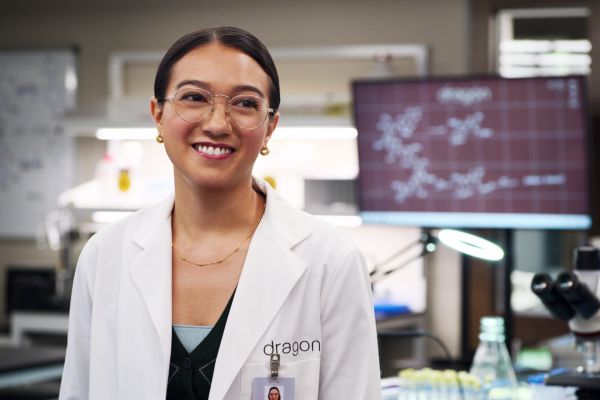 Luna steht im Labor und trägt einen weißen Laborkittel mit einem Lächeln im Gesicht