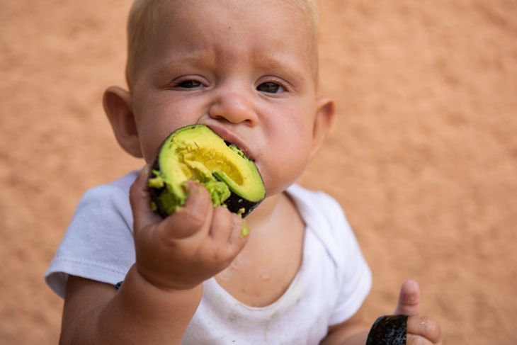Baby, das mit unordentlichen Händen eine Avocado isst