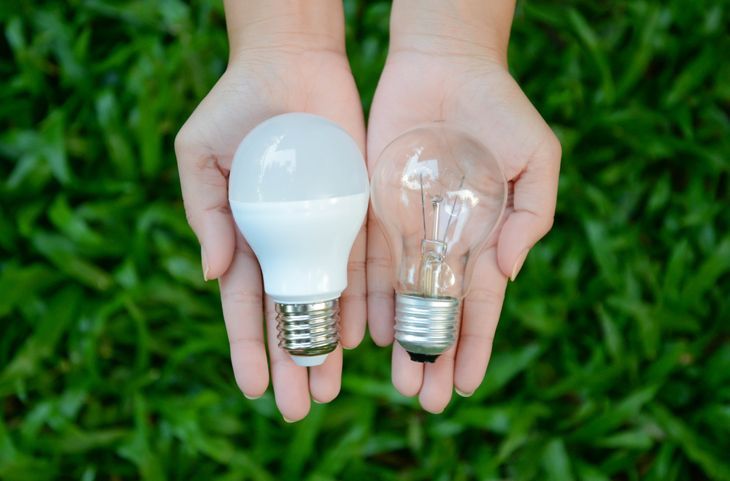 eine Frau, die in der einen Hand eine LED-Glühbirne und in der anderen eine Glühbirne hält