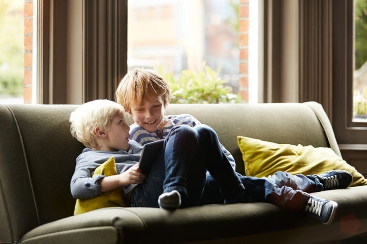 Aufnahme von zwei kleinen Brüdern, die mit einem digitalen Tablet auf ihrem Wohnzimmersofa sitzen