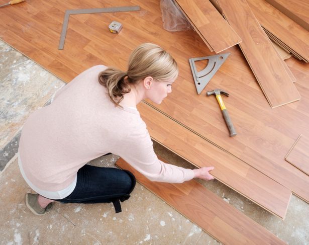 Eine Frau, die in ihrem Haus an einem Do-it-yourself-Projekt arbeitet, das Laminatboden verlegt. Sie platziert das Brett von oben gesehen.