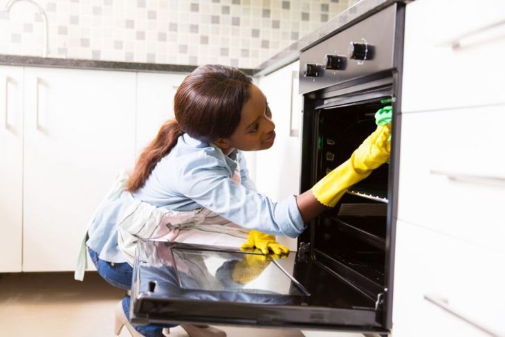 afrikanische Frau, die Herd in der modernen Küche putzt