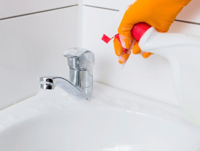 Person, die beim Reinigen des Waschbeckens und der Mischbatterie orangefarbene Gummihandschuhe trägt. Reinigungsservice.