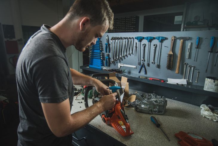 Professioneller Servicemann repariert eine Kettensäge mit einem Schraubenschlüssel, um die Schraube zu lösen. Mann repariert eine Kettensäge in einer schicken Werkstatt
