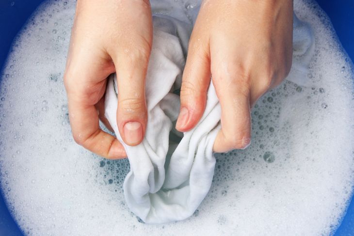 abgeschnittenes Bild von Händen, die ein weißes Hemd in Seifenwasser reinigen