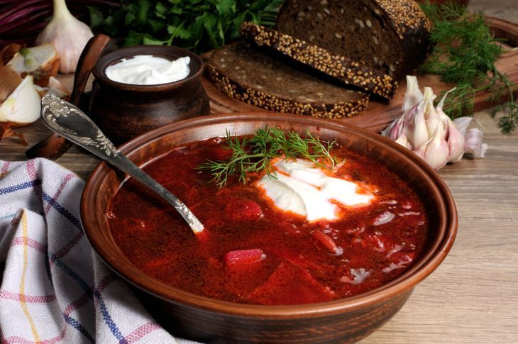 Borschtsch-Gemüse-Rote-Bete-Suppe, auf dem Tisch mit Scheiben Roggen-Müslibrot und Sauerrahm