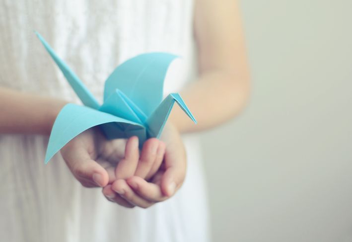 Kleines Mädchen, das einen blauen Origami-Vogel in ihren Händen hält