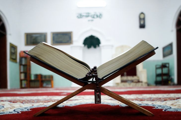 Ein offener Heiliger Koran und muslimische Gebetsperlen auf Holz stehen mit Mihrab im Hintergrund.