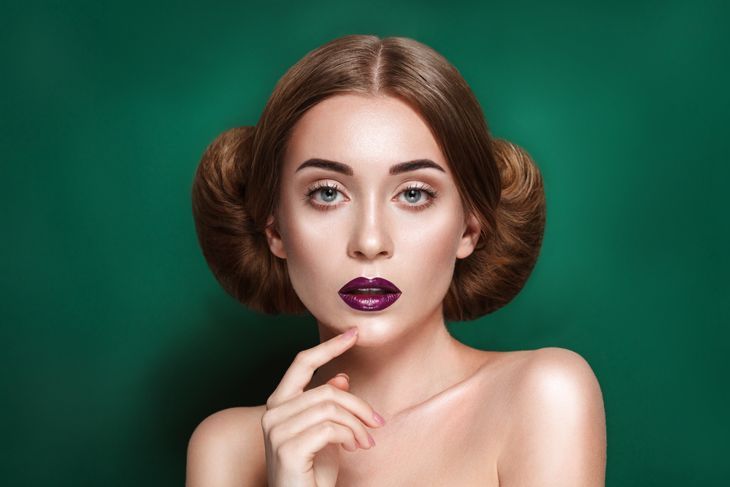Attraktive mysteriöse junge Frau mit doppeltem Haarknoten in Prinzessin Leia-Frisur schaut in Richtung der Kamera
